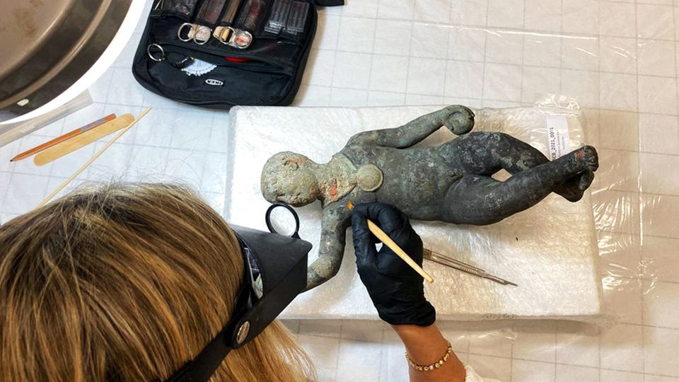 Une chercheuse étudie une figurine en bronze représentant un enfant